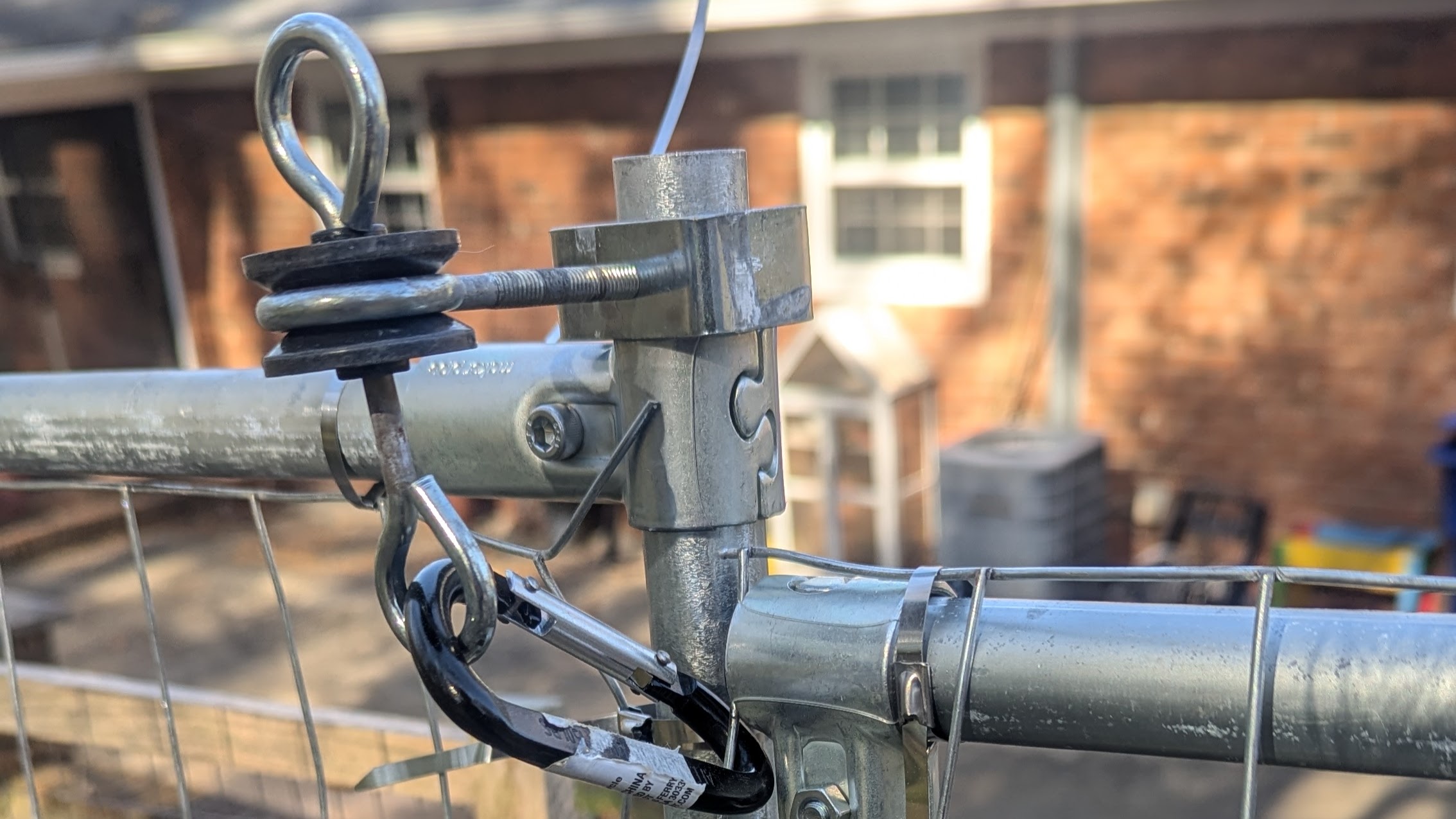 A close up of a fence gate latch made of a carabiner and an electric fence gate anchor.